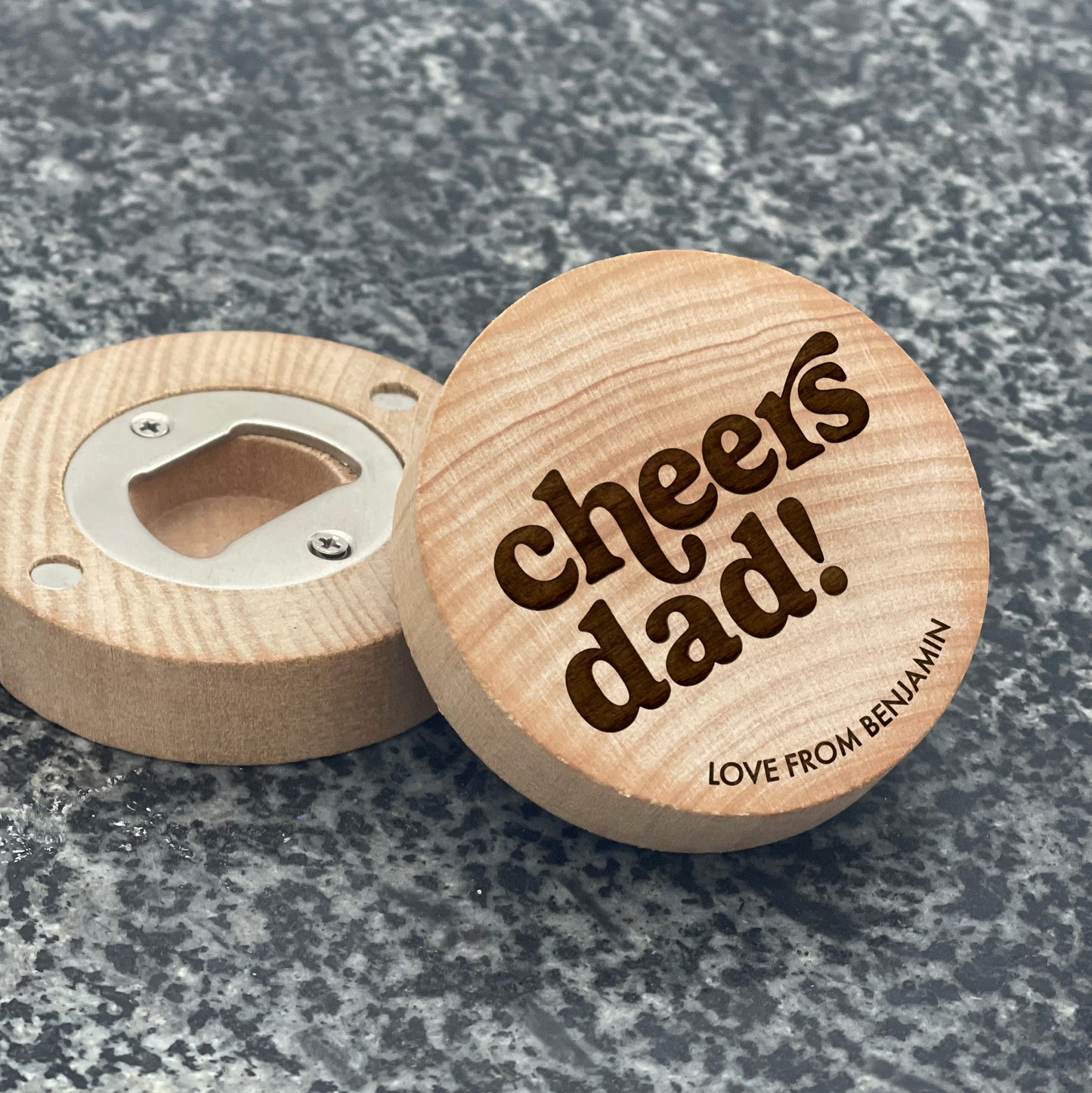 Father's Day Bottle Opener: cheers dad!. Pictured showing the engraved front and magnetic bottle opener back, on a stone countertop